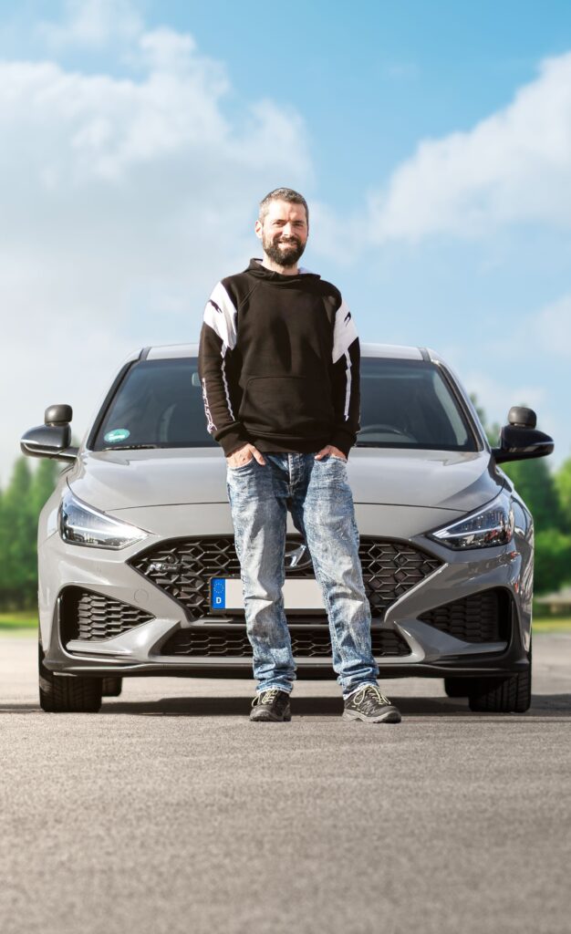 Dominik Heger, stehend vor dem Fahrschulauto